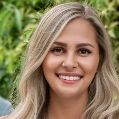 Blonde woman poses in front of foliage in a white shirt